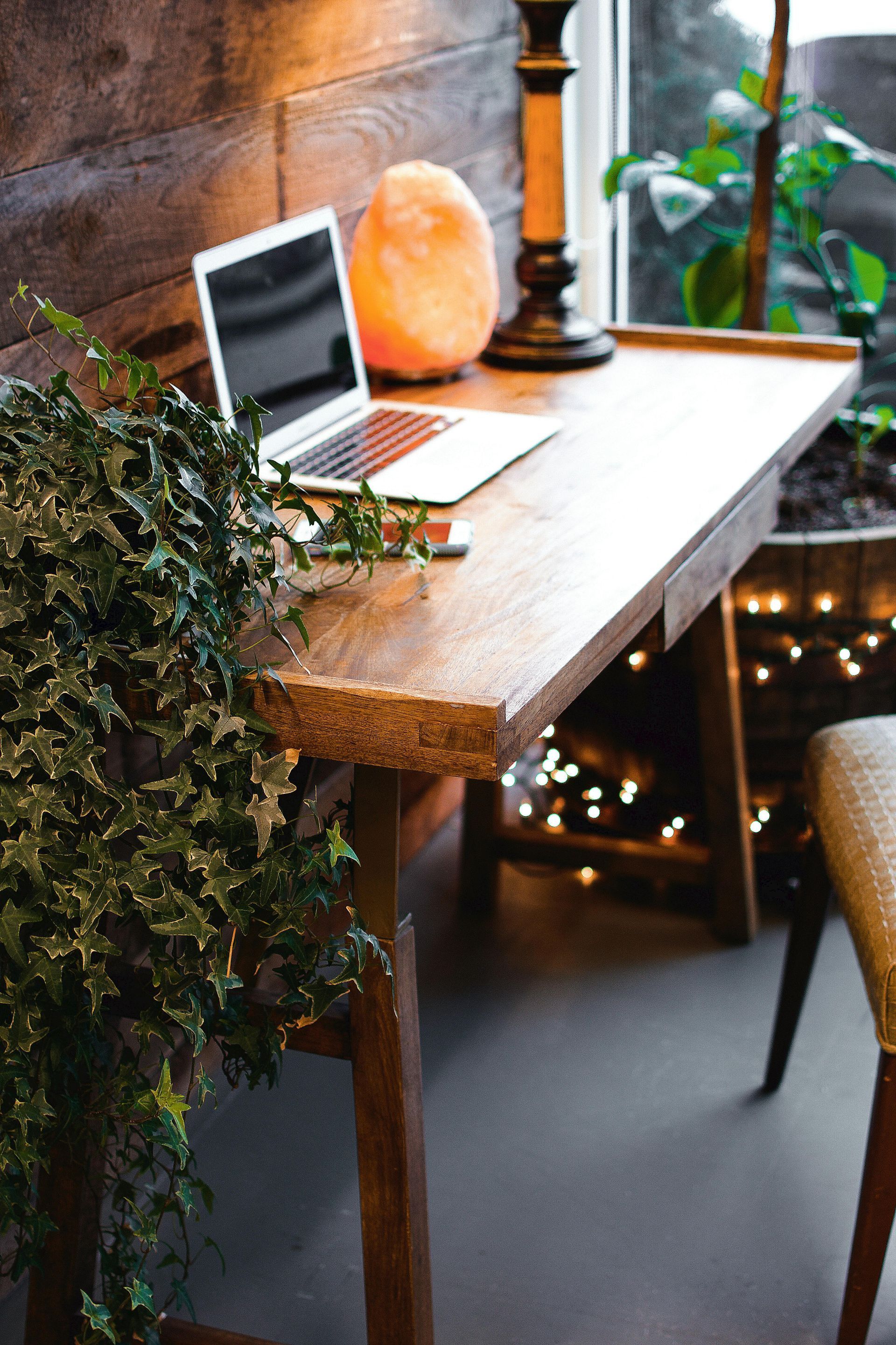 Cozy wooden home office desk with laptop, Himalayan salt lamp, and ivy plan