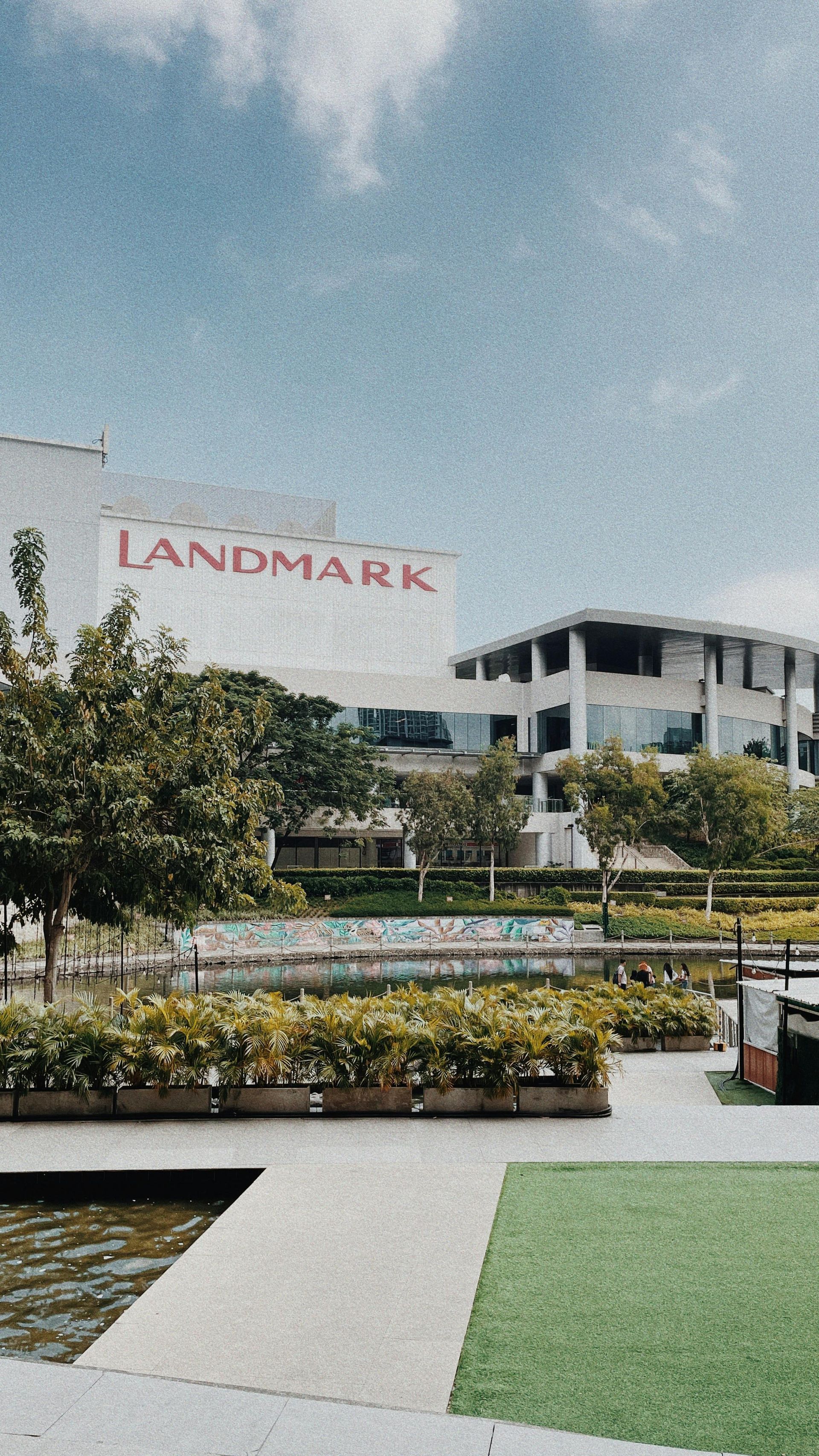 Landmark building with red logo, water feature, and greenery against a cloudy sky.