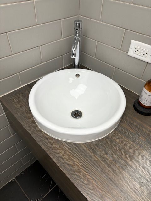 A white sink is sitting on a wooden counter in a bathroom.