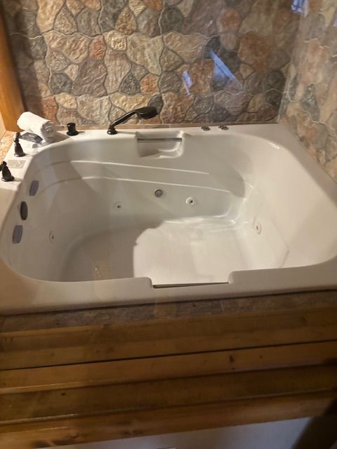 A large white jacuzzi tub is sitting in a bathroom next to a stone wall.