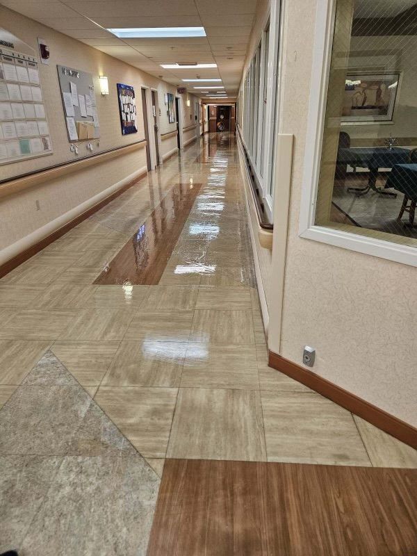 A long hallway in a hospital with wooden floors and a window.
