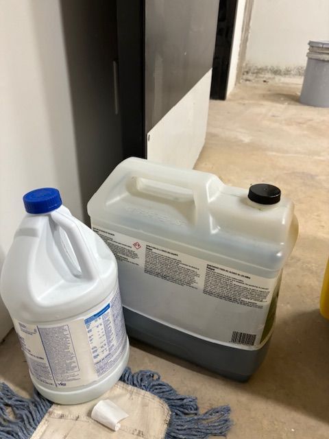A bottle of bleach is next to a cooler and a mop