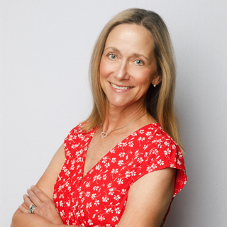 A woman wearing a blue shirt and a heart necklace is smiling for the camera.