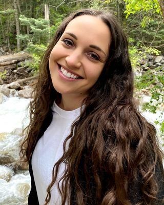 a woman with long brown hair is smiling in front of a river .
