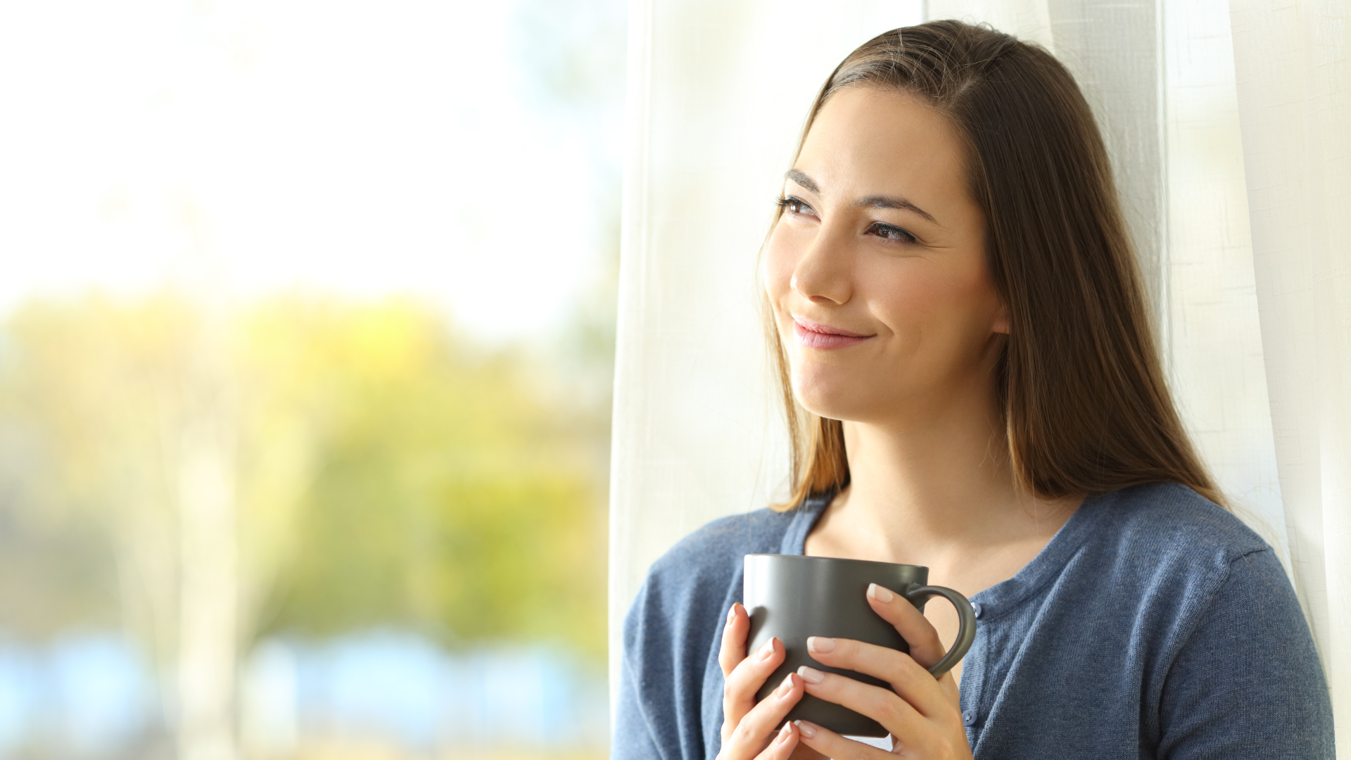 a woman is holding a cup of coffee and looking out of a window .