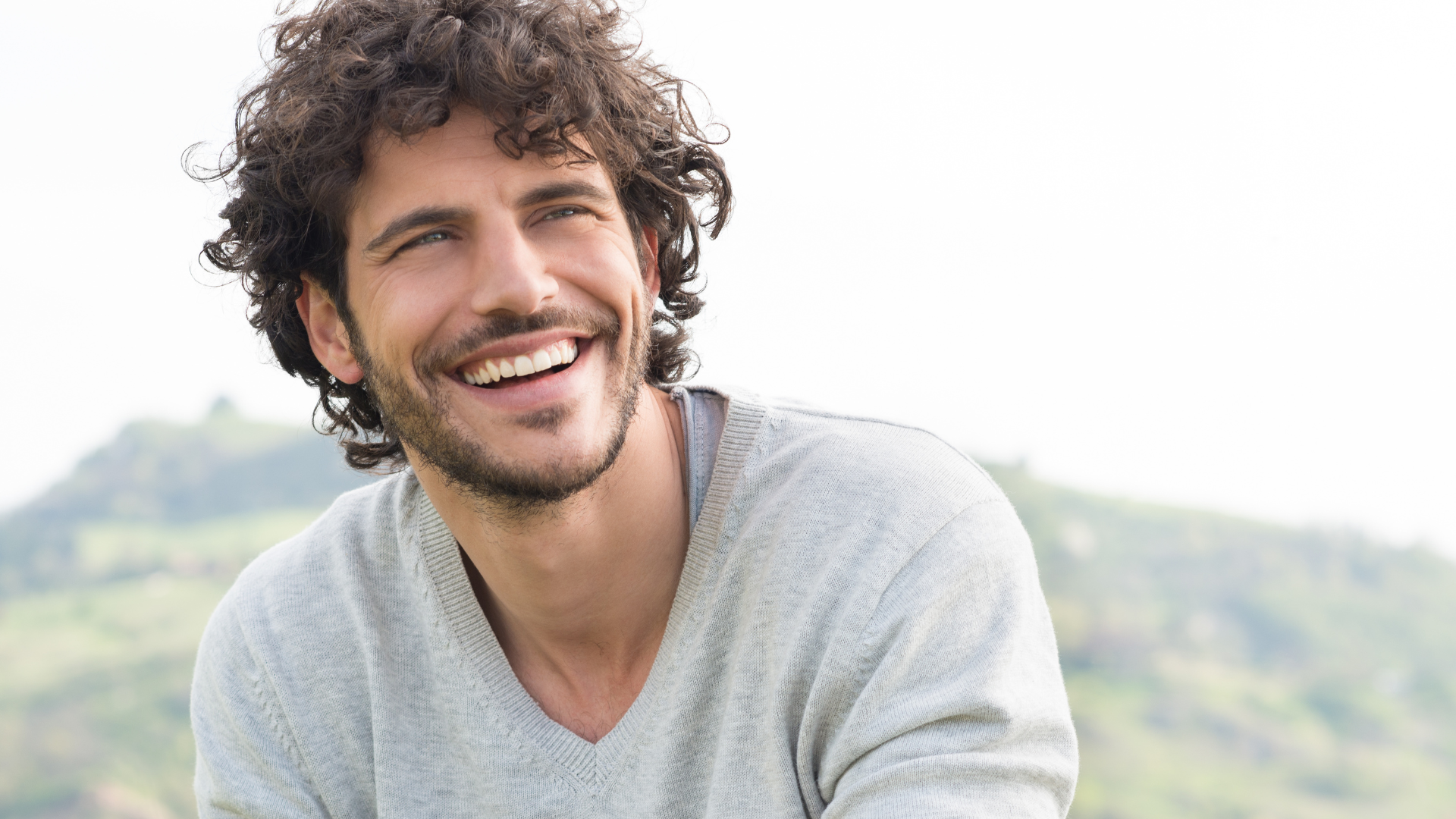 a man with curly hair and a beard is smiling .