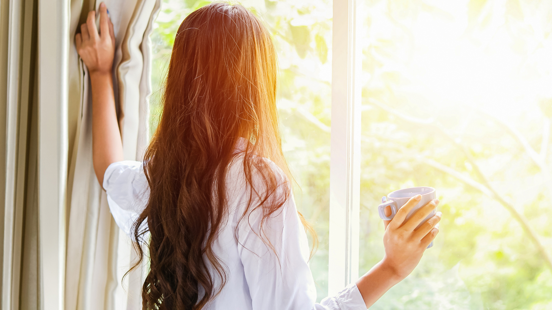 a woman is standing in front of a window holding a cup of coffee .