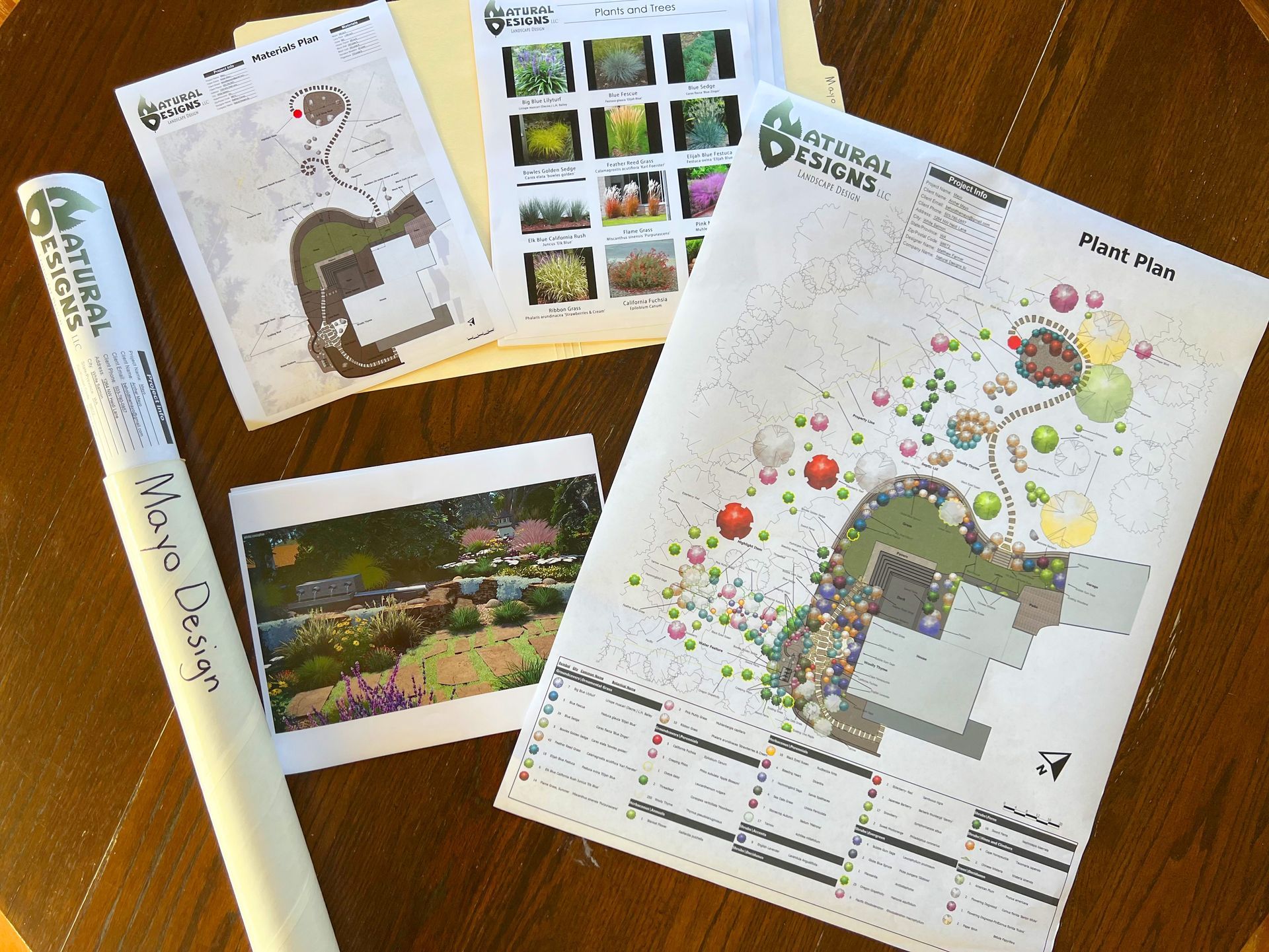 Landscape design plans and photo, including a rolled drawing, on a wooden table.