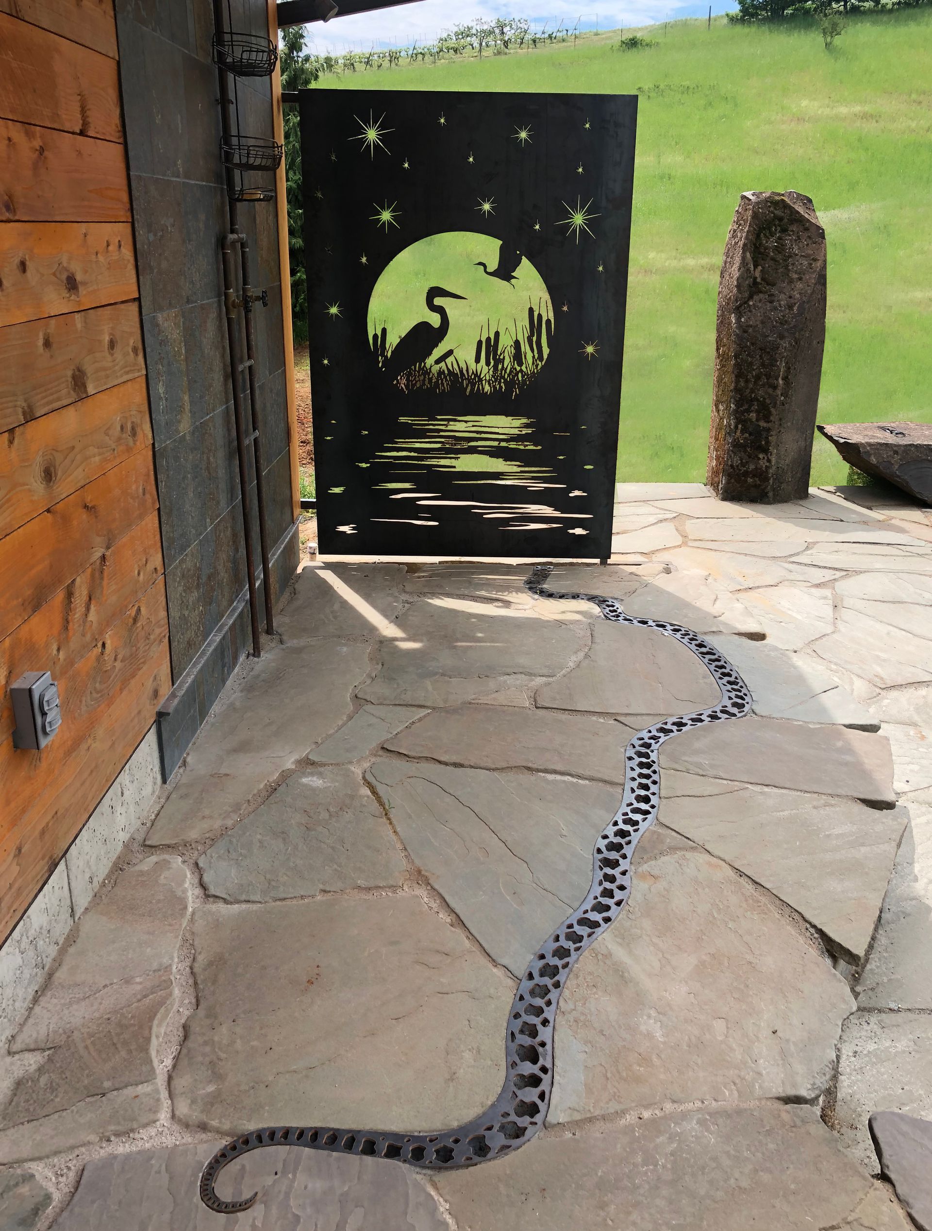 Stone path beside a wooden building, leading to a black gate with a green bird design