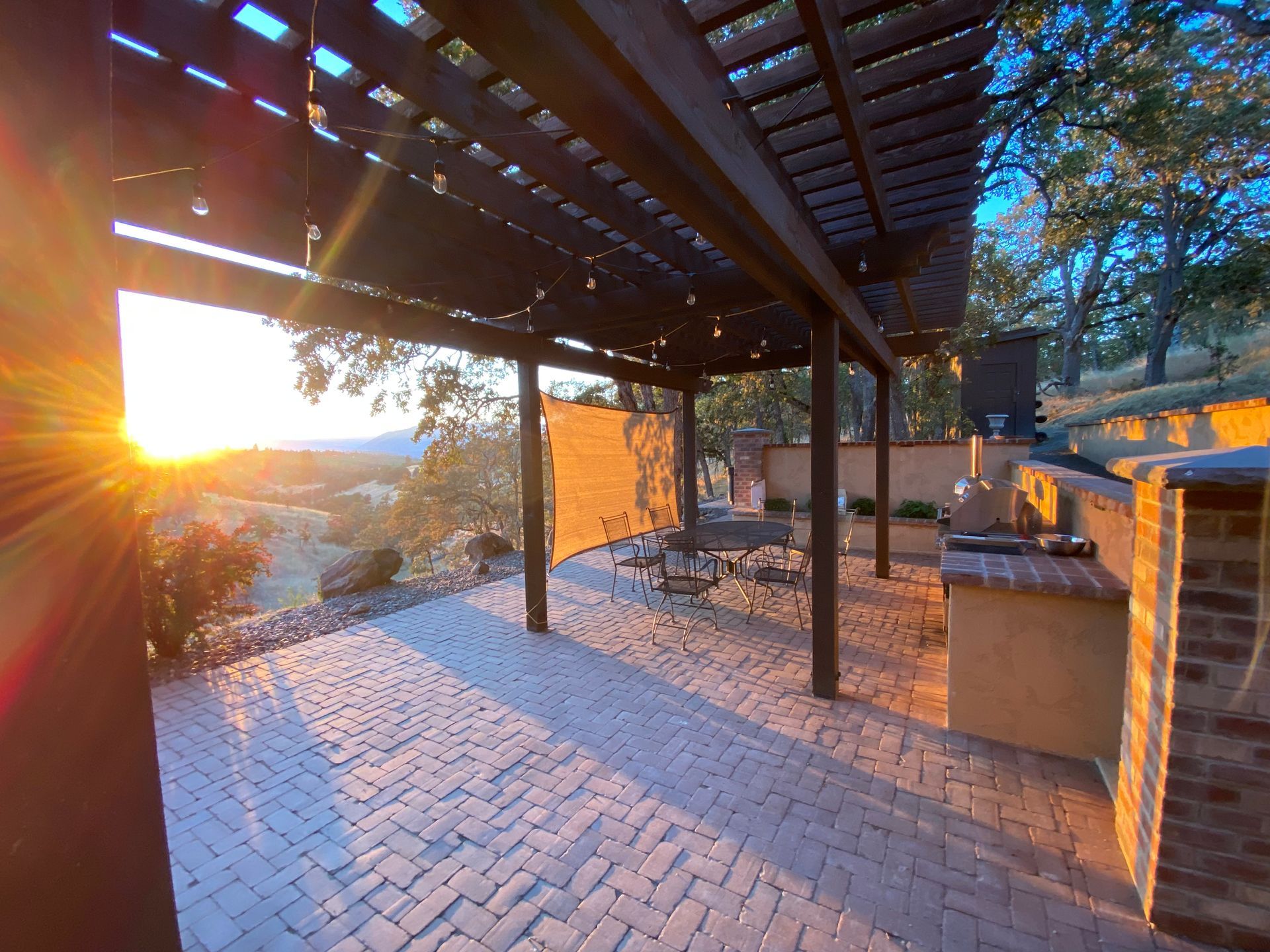 Sunlit patio with pergola, brick floor, and hillside view at sunset