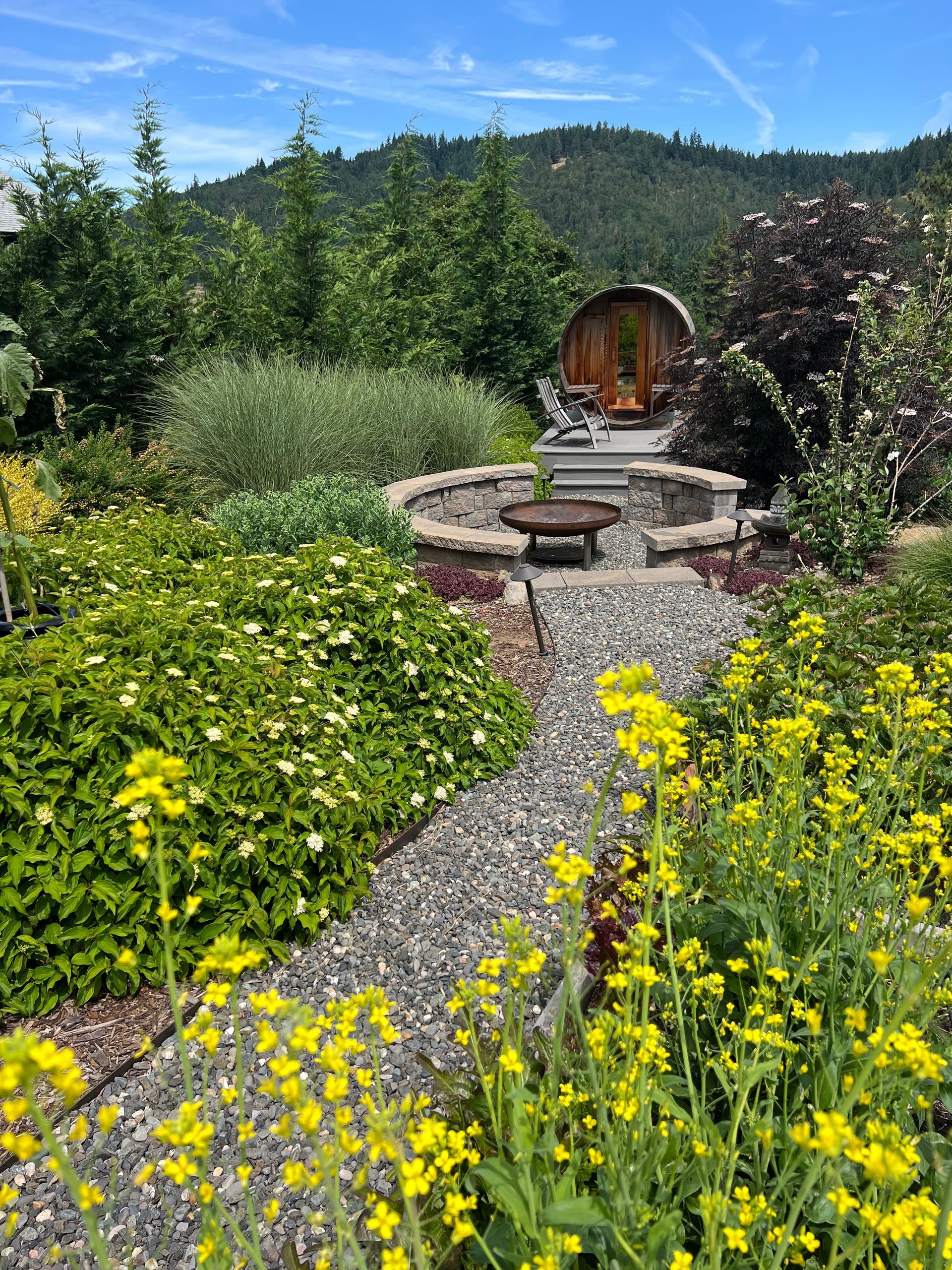 A vibrant garden with a stone path leading to a fountain and hillside backdrop. Yellow flowers in foreground.