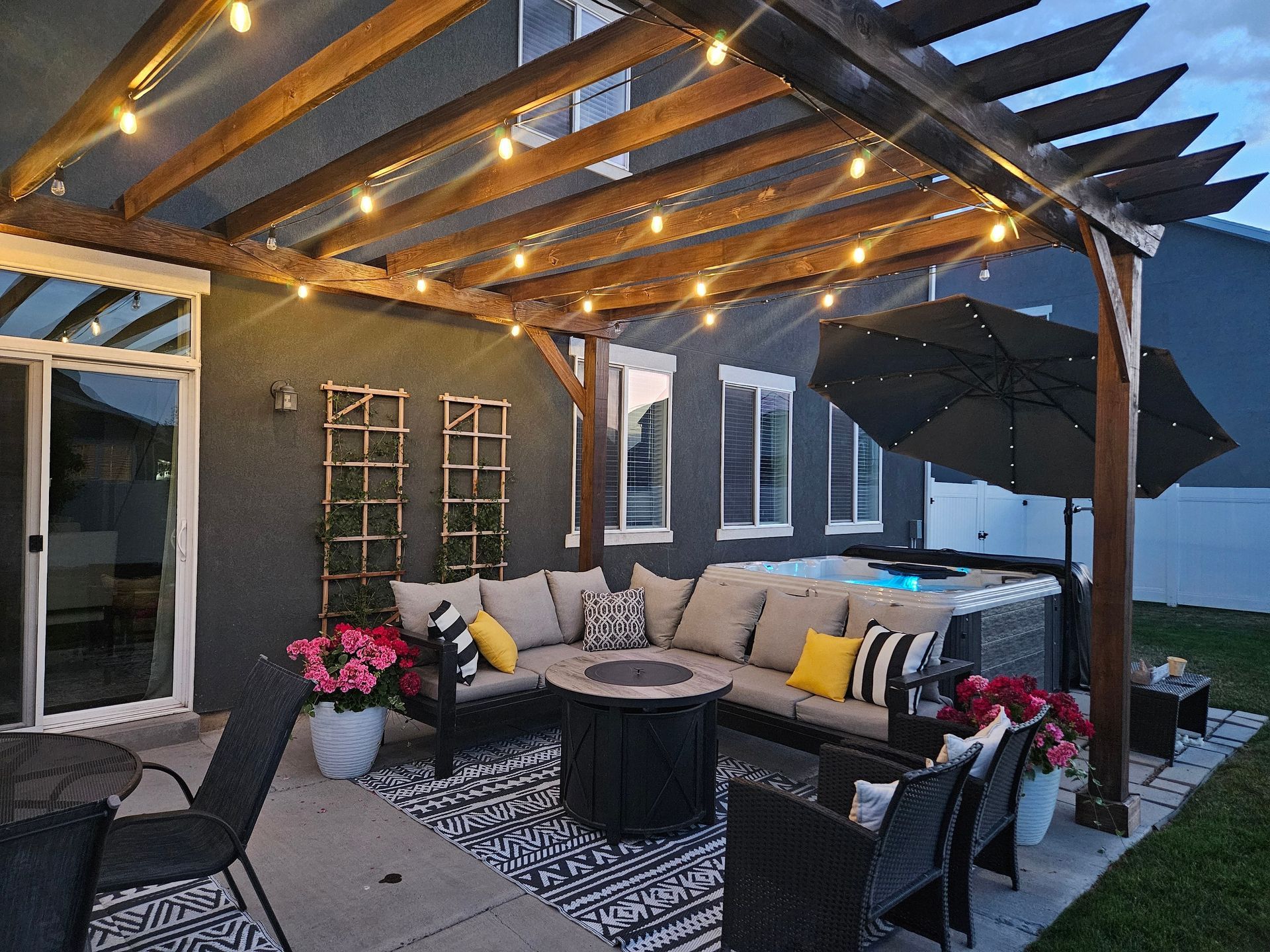 Covered patio with string lights, sectional seating, fire pit, and umbrella at dusk