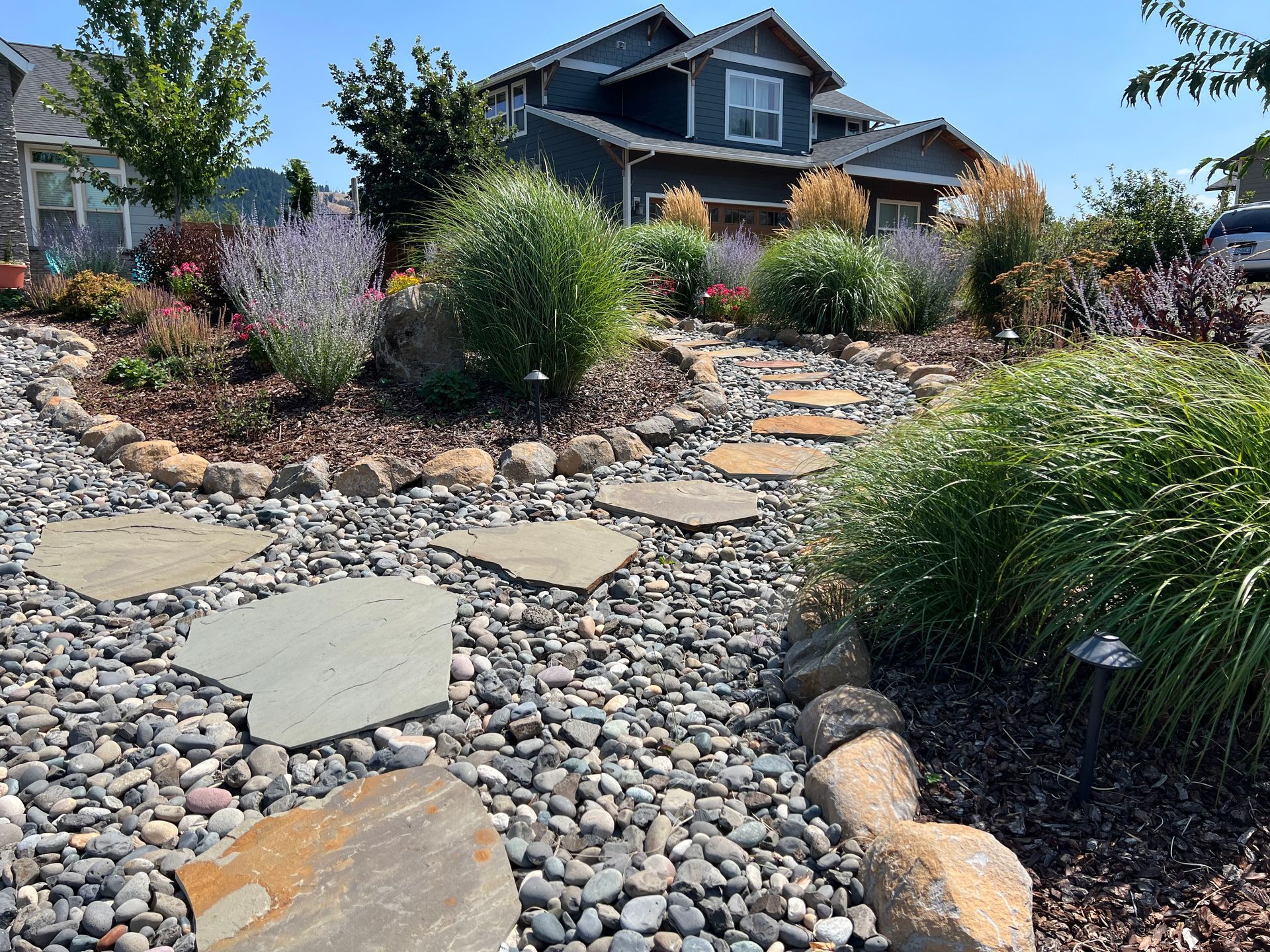 Stone path leads through a landscaped yard with a dark blue house in the background.