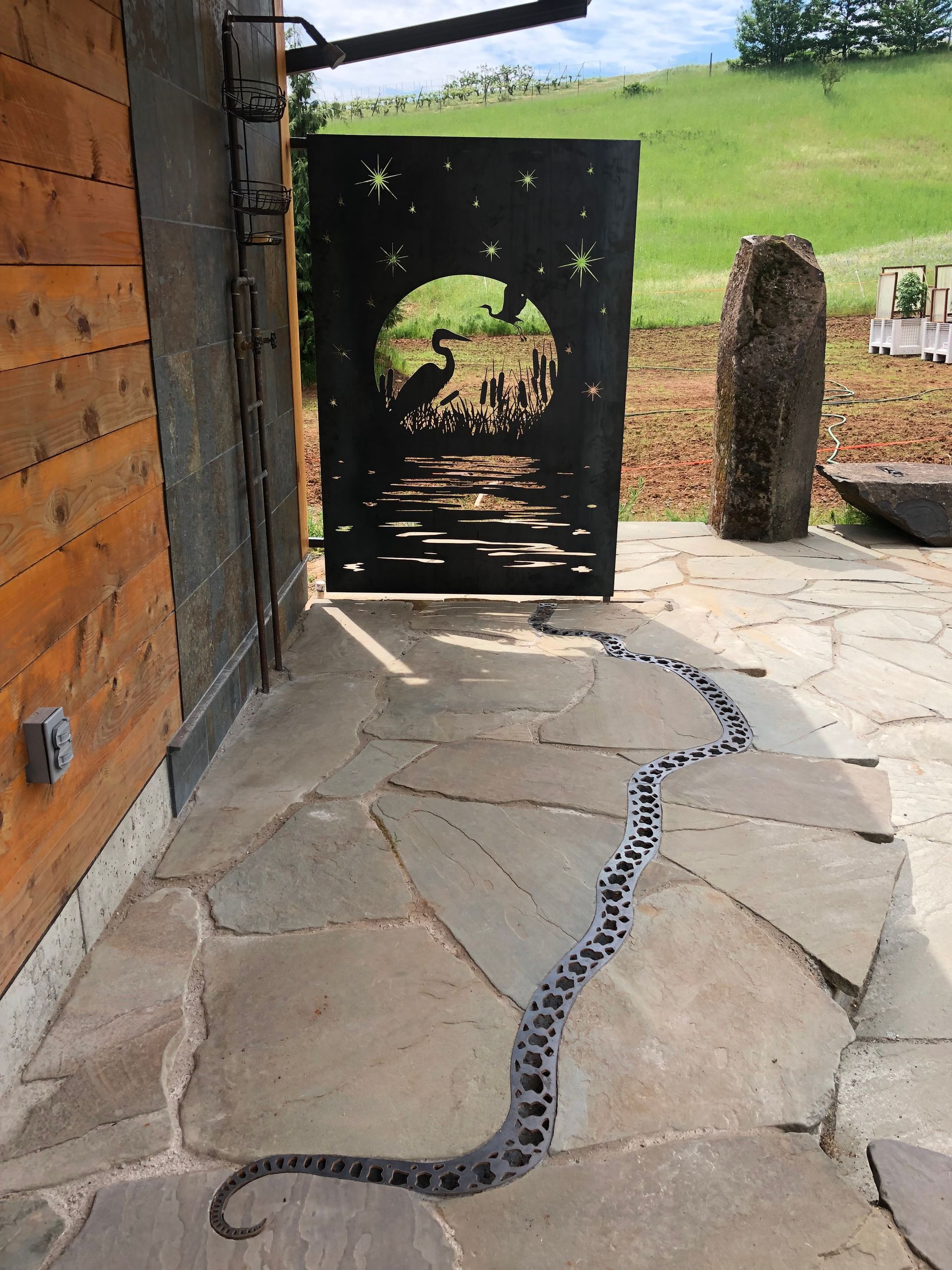 A snake is crawling along a stone walkway next to a wooden wall