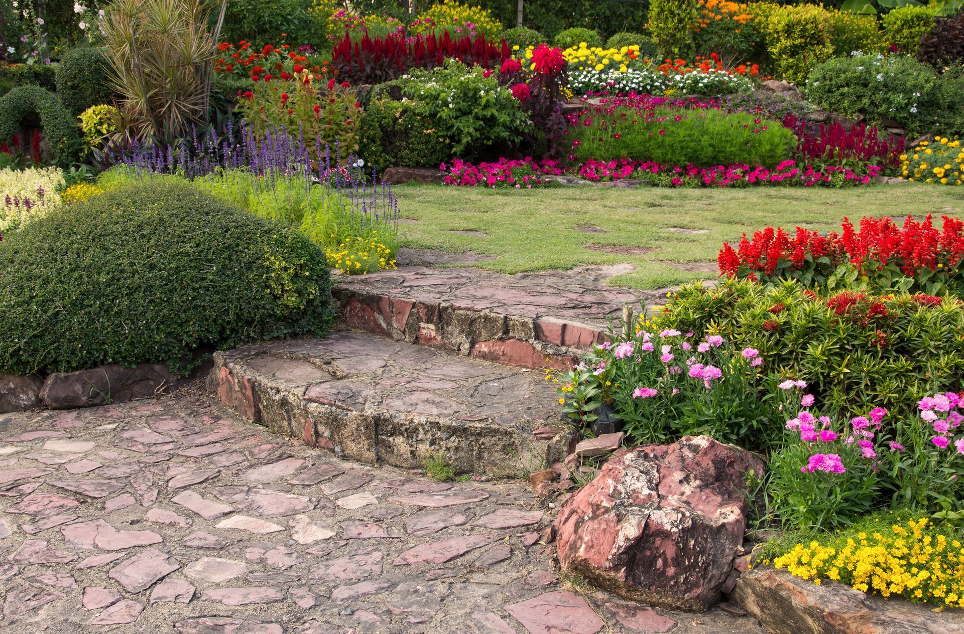 Stone steps lead up to a colorful tiered garden with vibrant flowers and greenery.