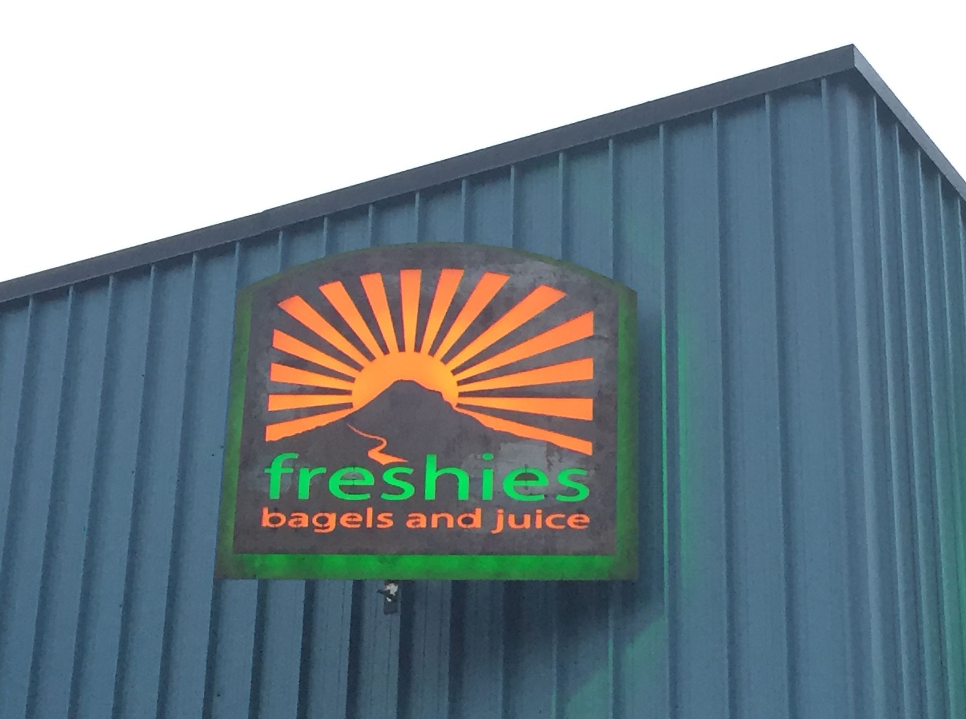 Sign for Freshies Bagels and Juice with a rising sun over a mountain, on a teal building.