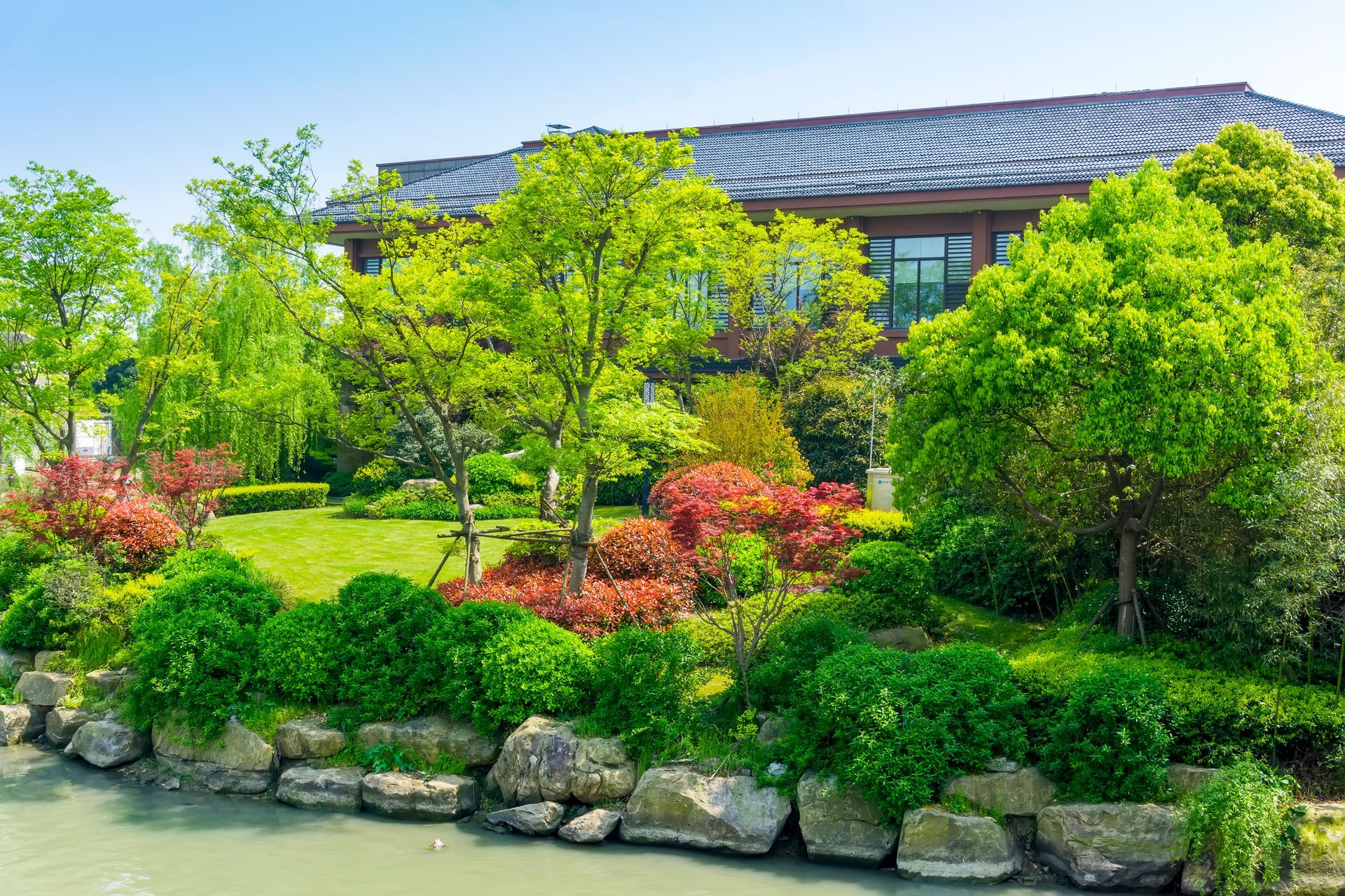 A large house is surrounded by a lush green garden and a river.