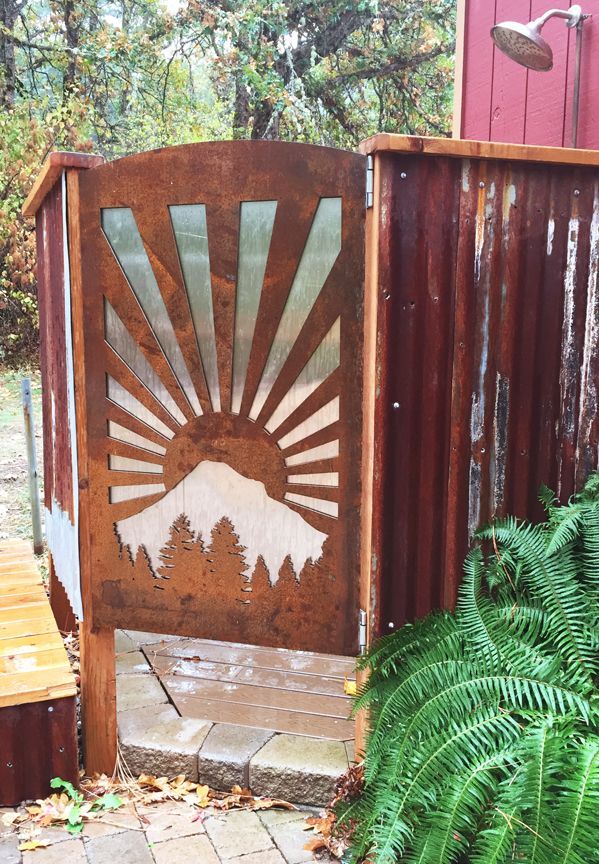 Outdoor shower with rusty corrugated metal walls and a sunrise cut-out design.