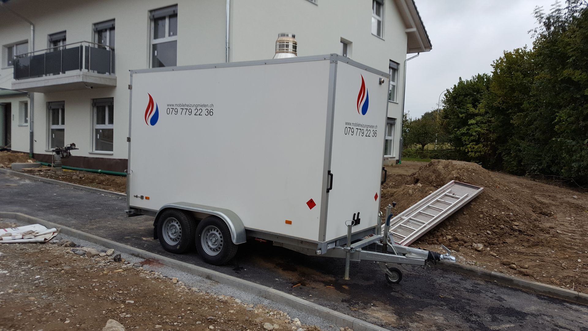 Ein weißer Anhänger steht vor einem im Bau befindlichen Haus.