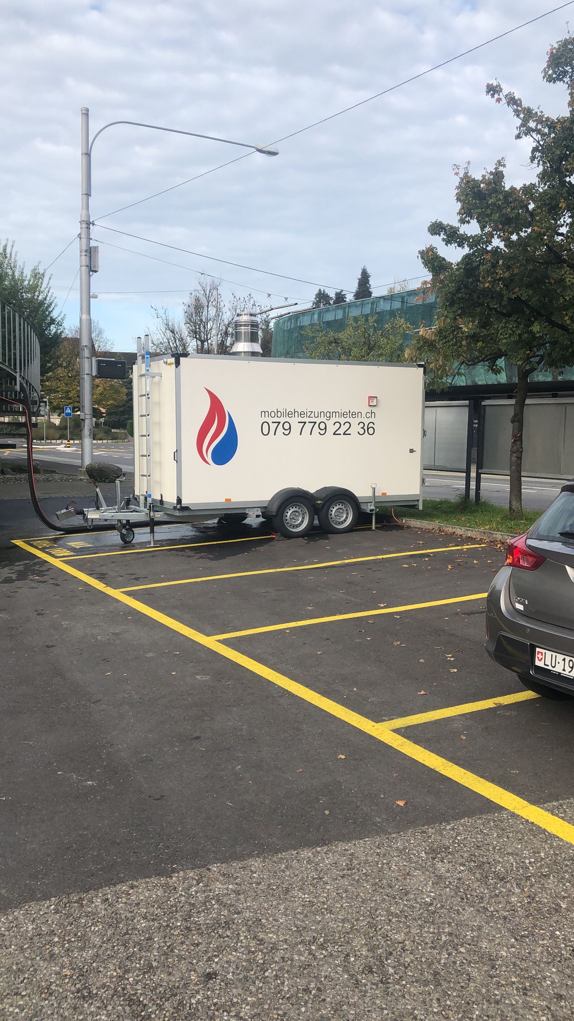 Ein weißer Anhänger steht auf einem Parkplatz neben einem Auto.