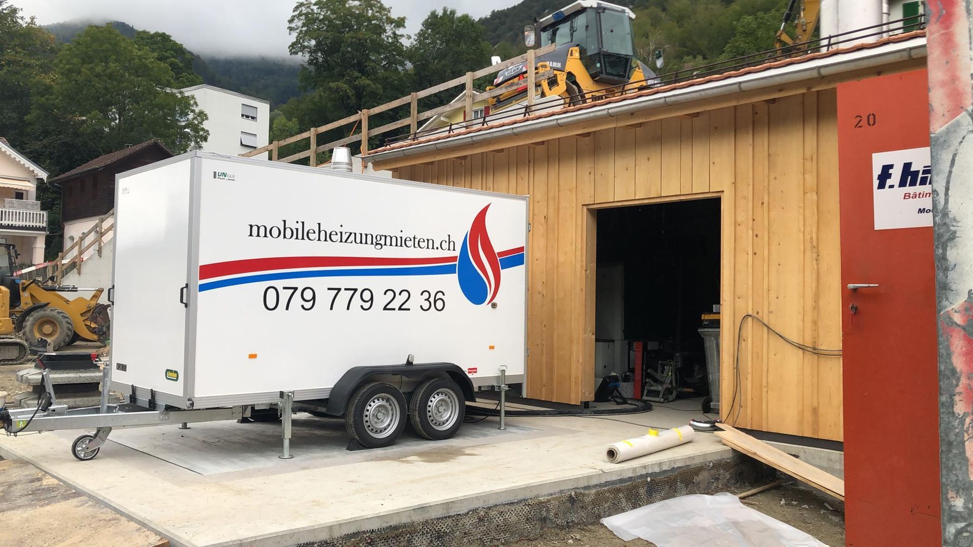 Ein weißer Anhänger steht vor einem Holzgebäude.