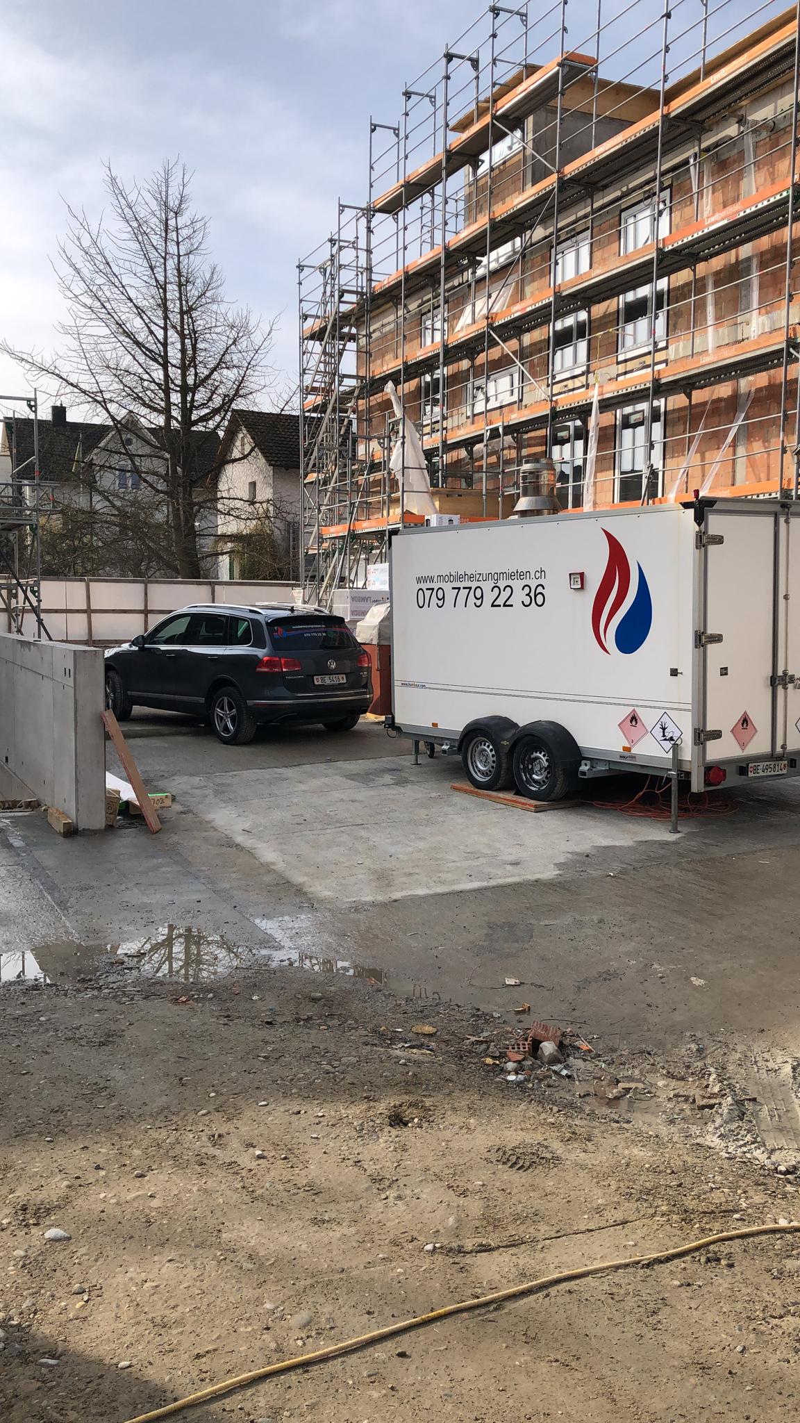 Ein weißer Anhänger steht vor einem im Bau befindlichen Gebäude.