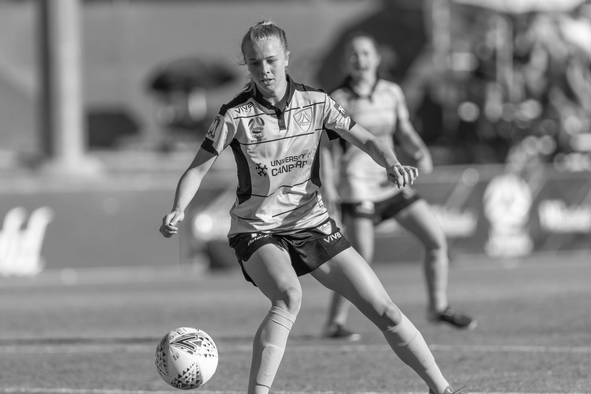 Soccer player in yellow and black uniform dribbling a ball on a sunny field.