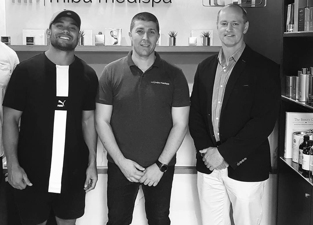 Three men posing inside a shop. One in black shirt, one in a red polo, and one in a blazer.
