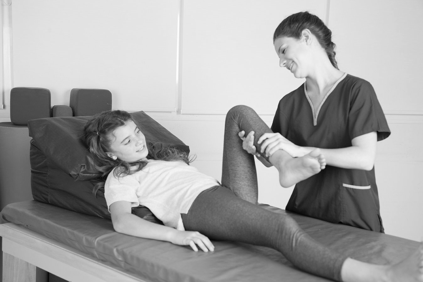 Therapist assisting a patient with leg movement on an examination table.