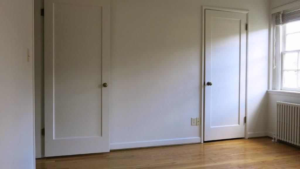 An empty room with two white doors and a window.