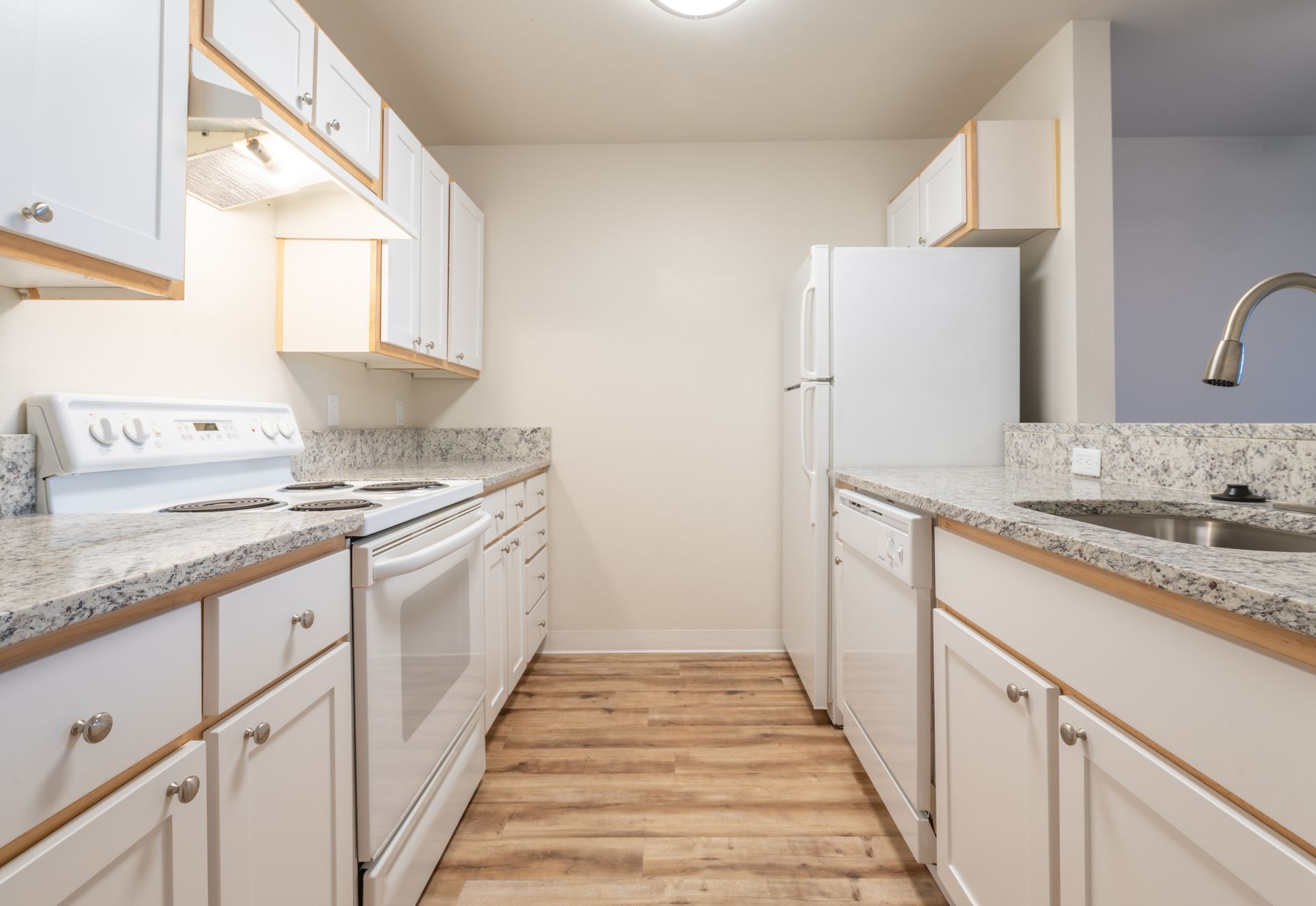 A kitchen with white cabinets , a stove , a refrigerator , and a sink.