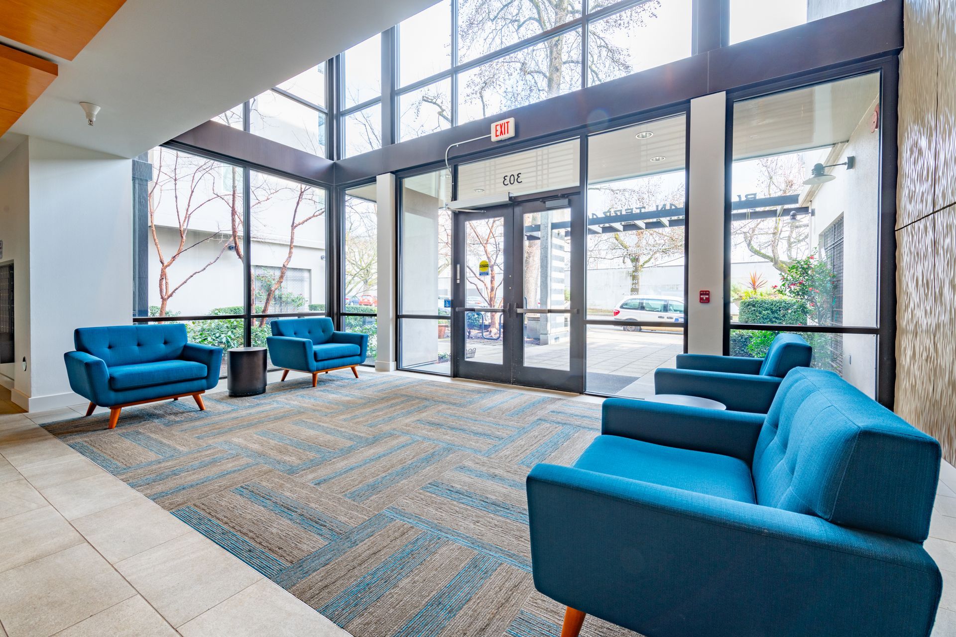 A lobby with blue chairs , a couch , and a large window.