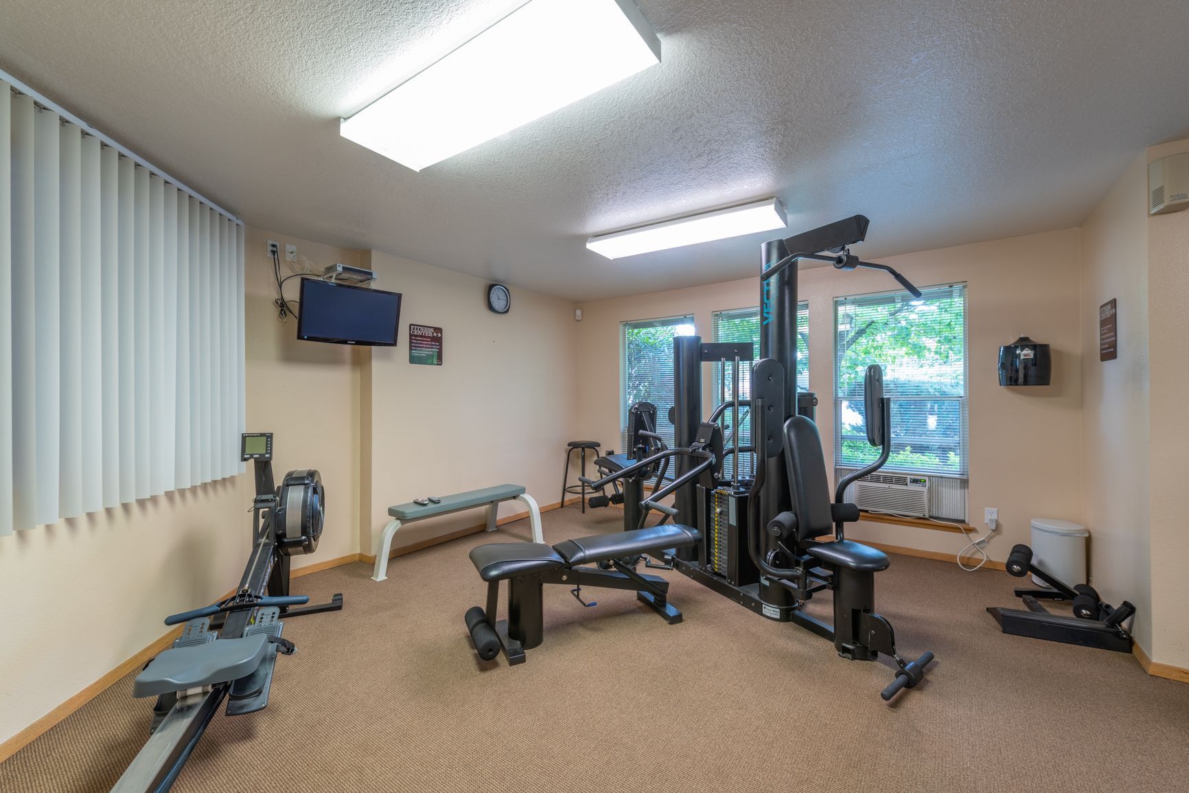 A gym with a lot of exercise equipment and a television on the wall.