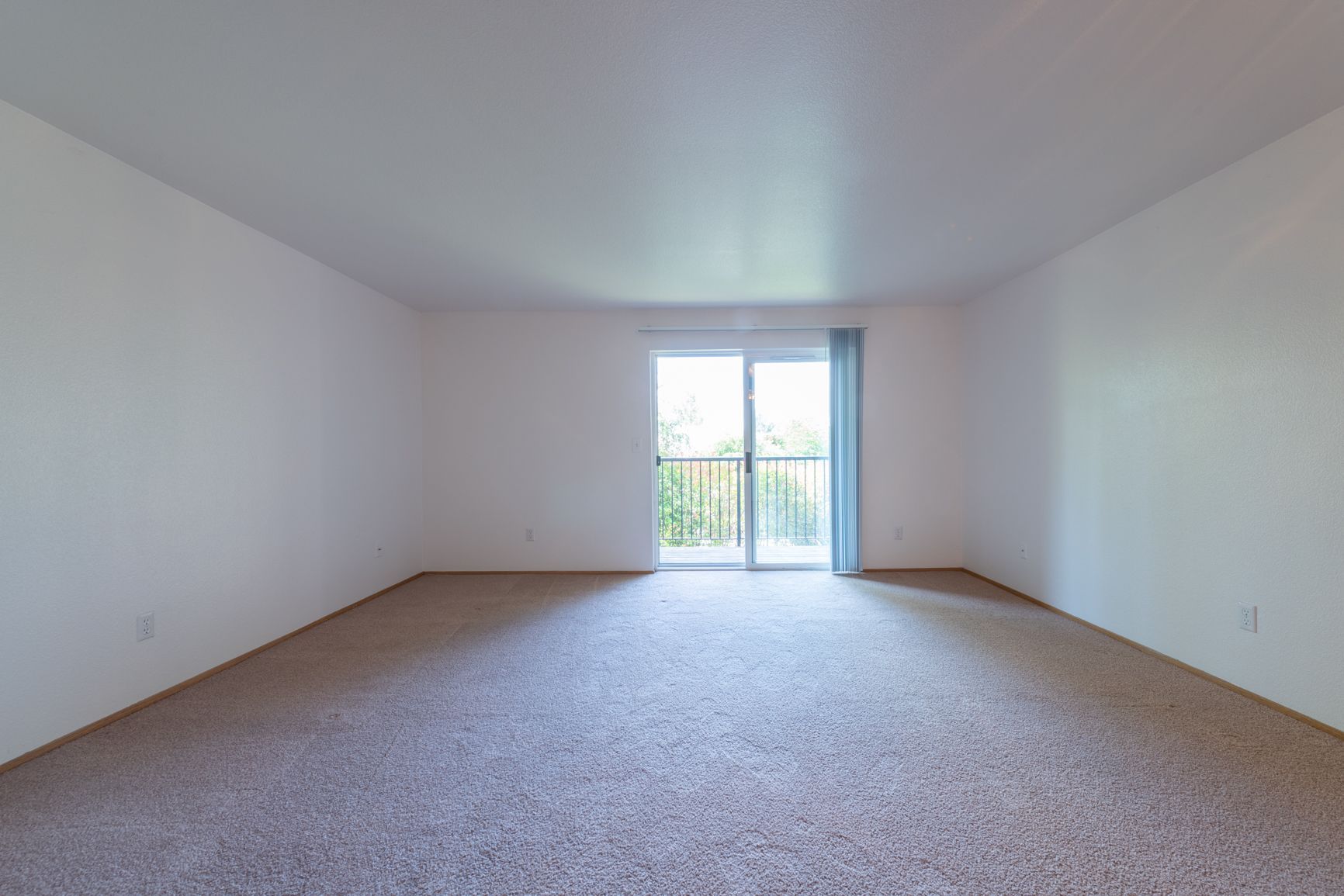 An empty living room with a balcony and sliding glass doors.
