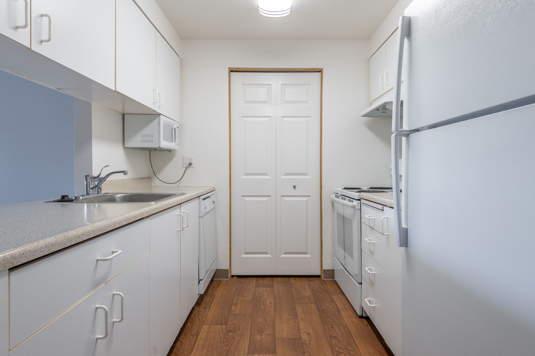 A kitchen with white cabinets , a refrigerator , a stove , and a sink.