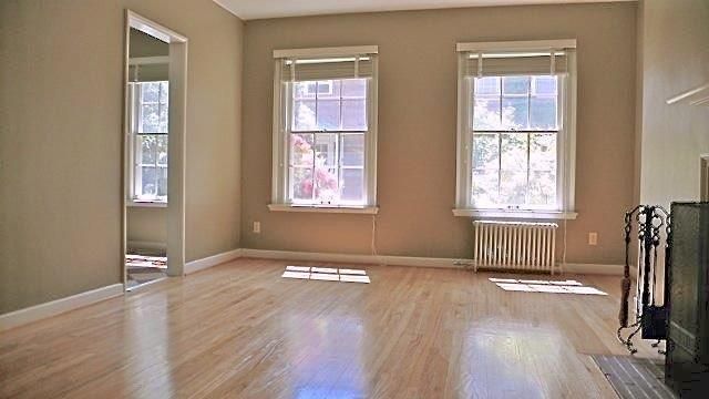 An empty living room with hardwood floors and two windows.