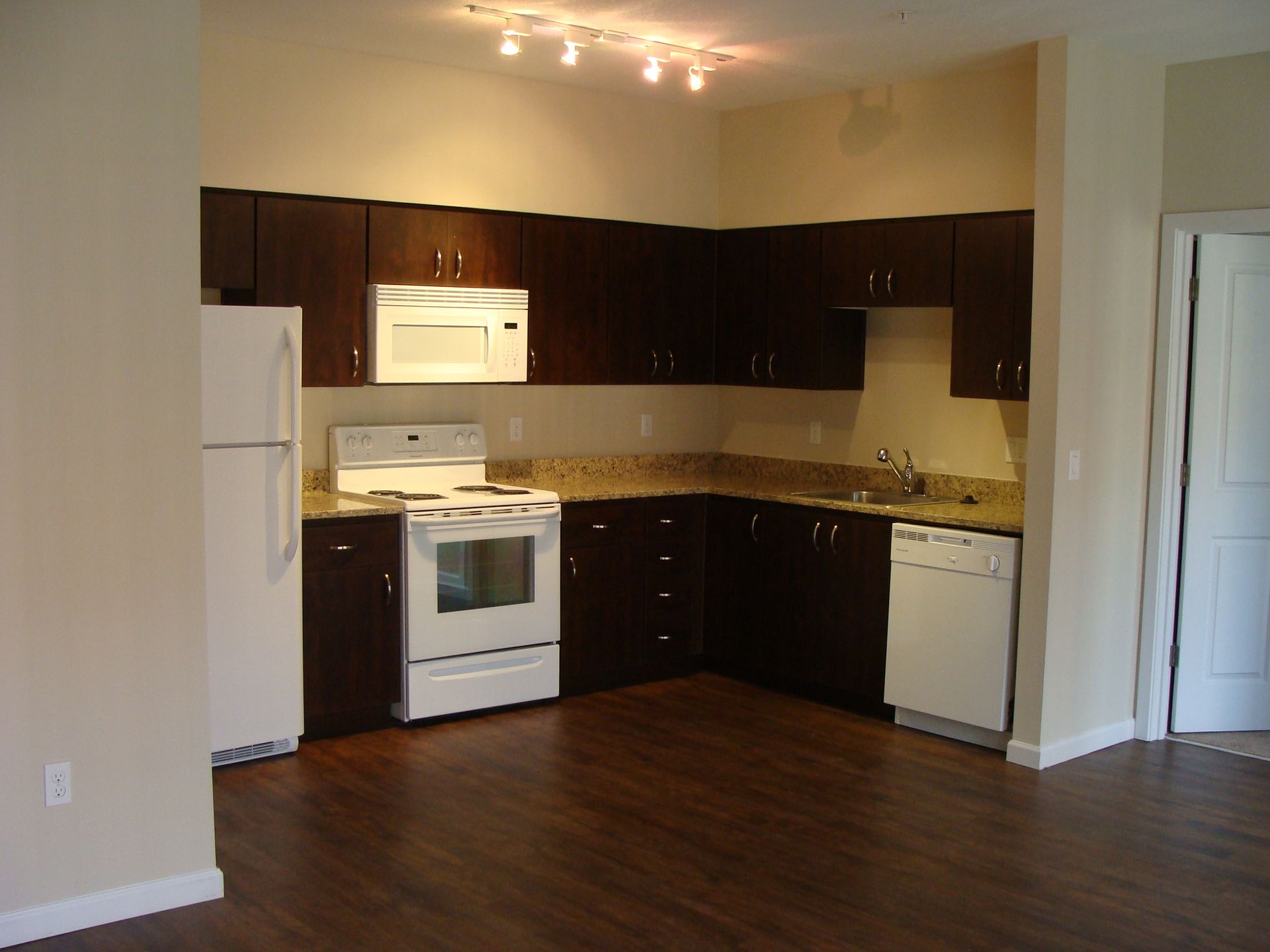 An empty kitchen with brown cabinets and white appliances
