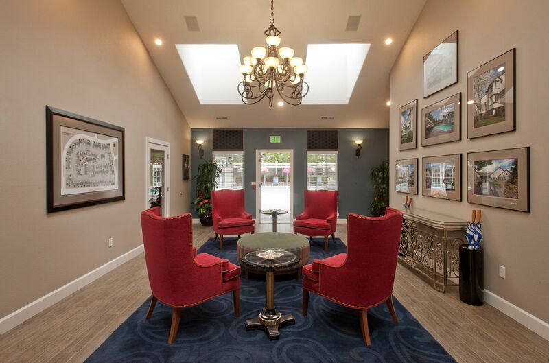 A living room with red chairs , a table and a chandelier.