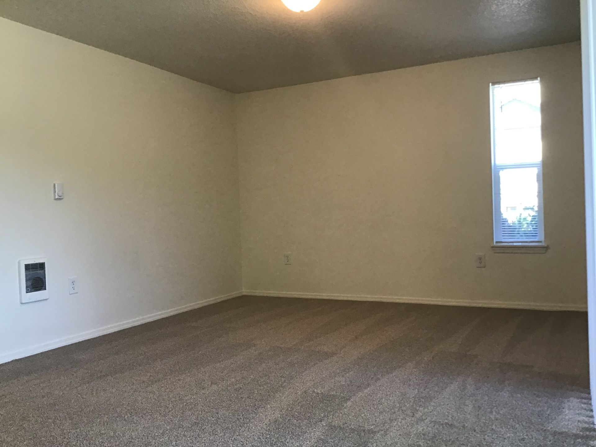 An empty living room with a carpeted floor and a window.