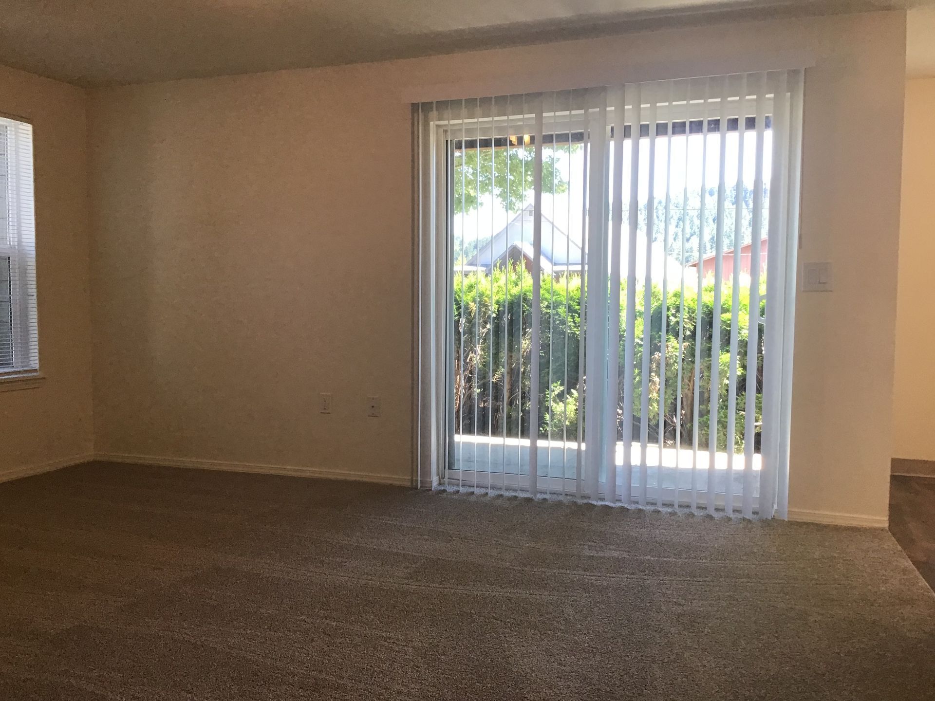 An empty living room with sliding glass doors and blinds.
