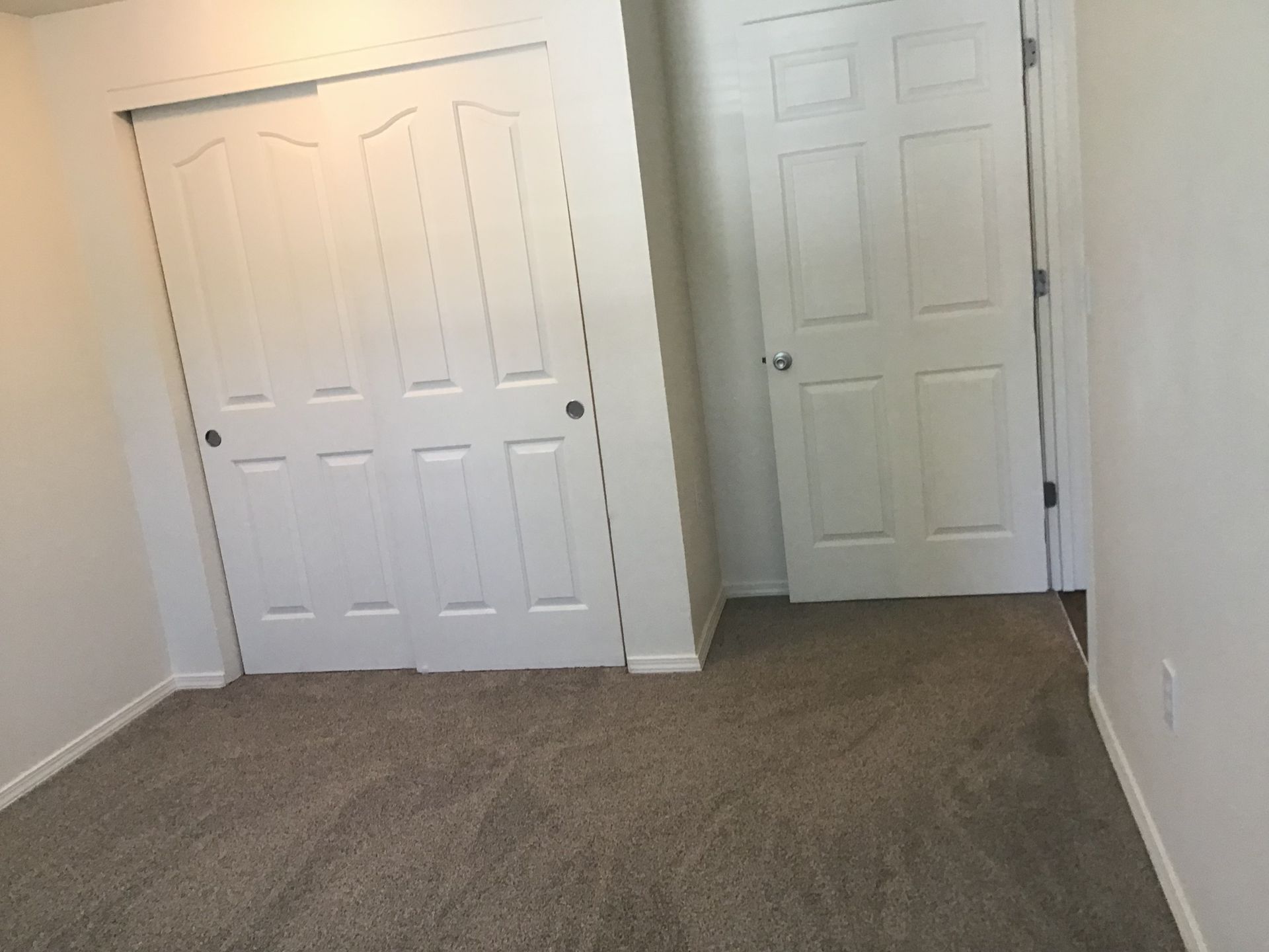 An empty bedroom with a closet and two doors.