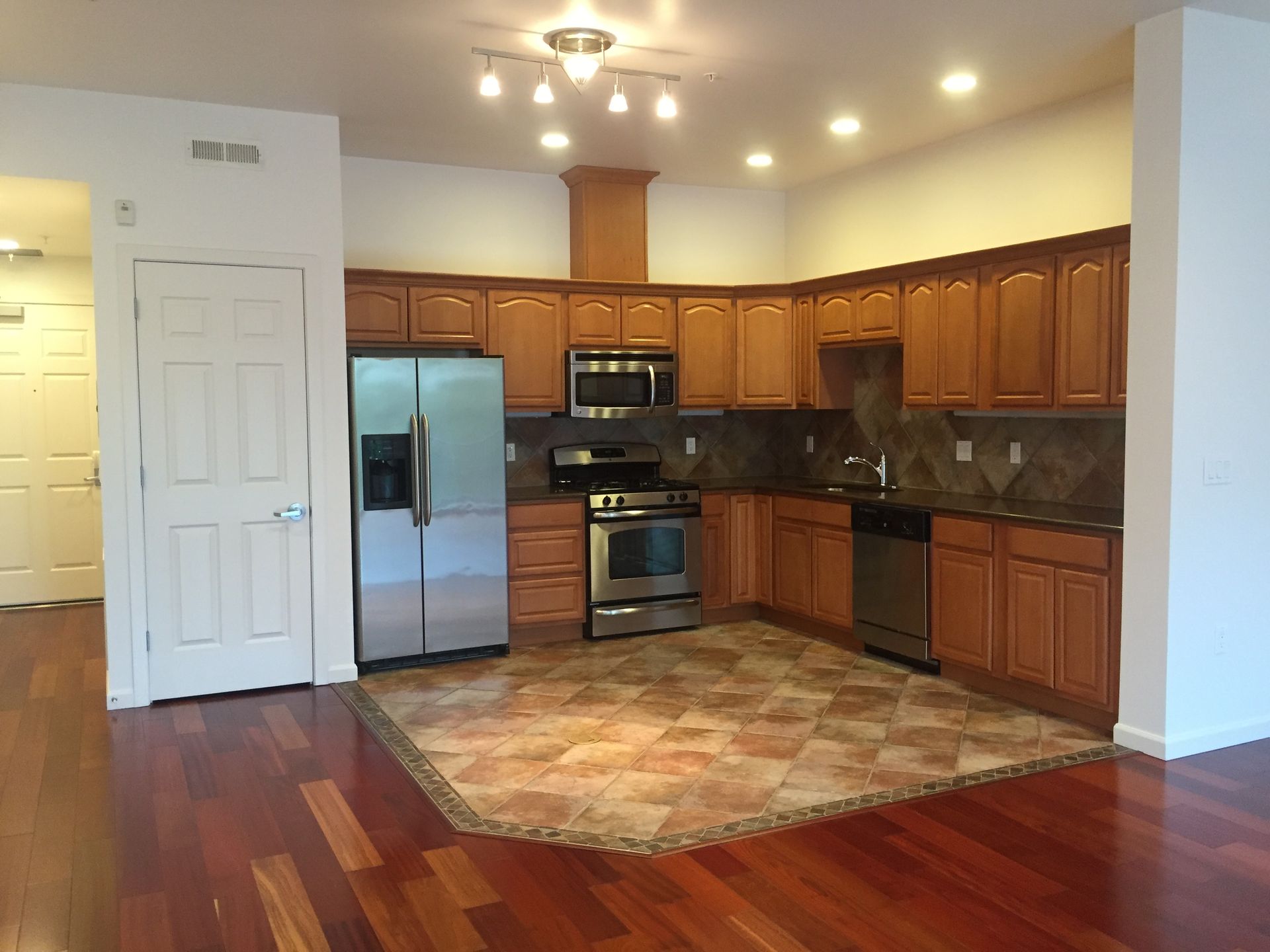 An empty kitchen with wooden cabinets and stainless steel appliances
