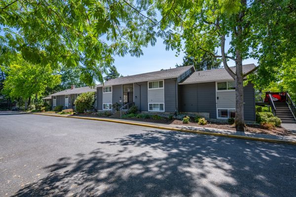 A row of apartment buildings with trees in front of them on a sunny day.