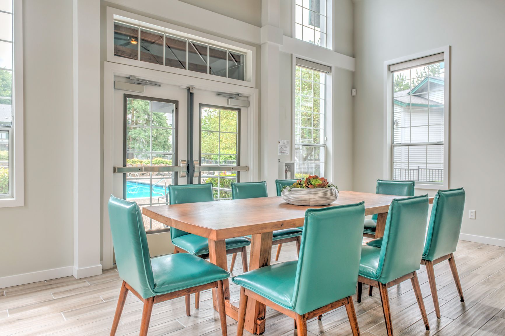 A dining room with a table and chairs and a pool in the background.