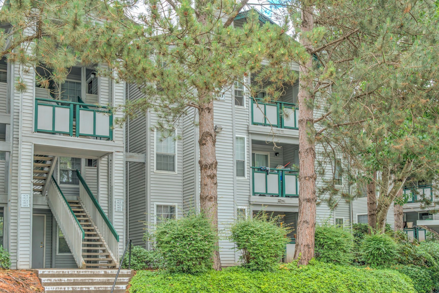 A large apartment building with stairs leading up to the second floor surrounded by trees.