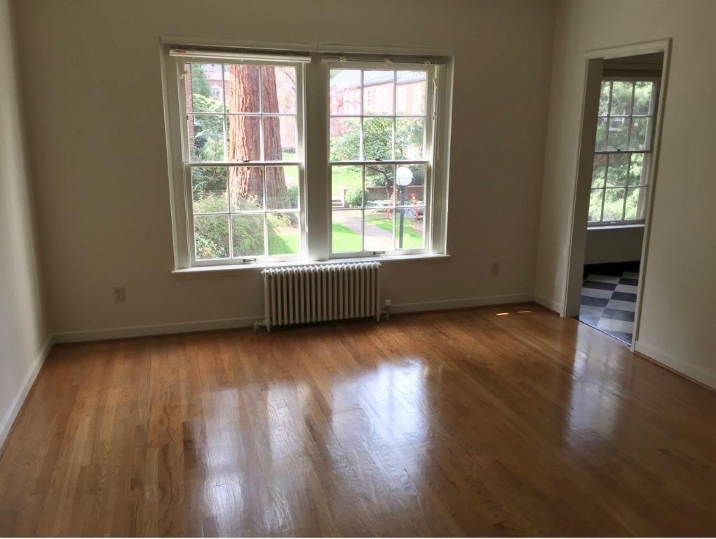 An empty living room with hardwood floors and two windows.