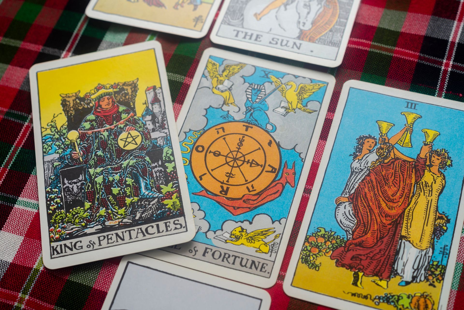 A group of tarot cards on a table including the king of pentacles and the sun