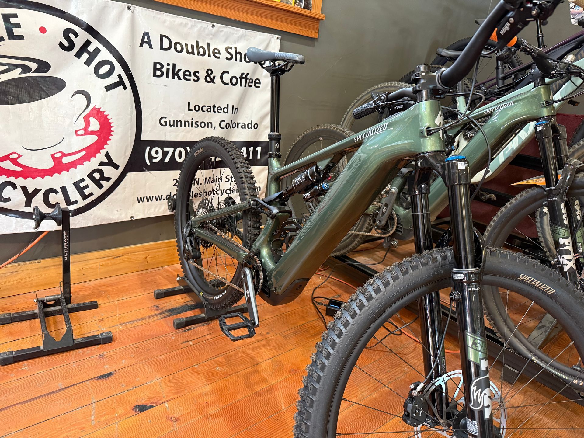 A bicycle is parked in front of a sign that says a double shot bikes & coffee.