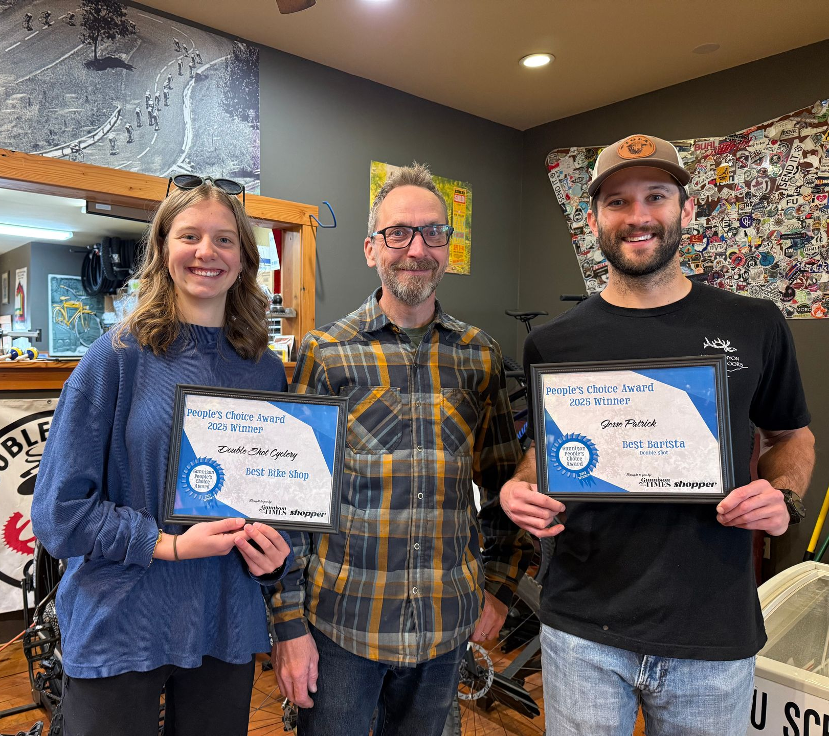 Three people holding awards in a shop. The people smile. Blue and white awards.