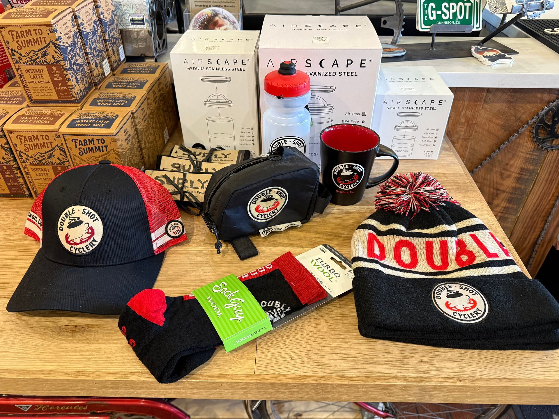 Merchandise display: hats, mug, water bottle, and socks with "Double Shot" logo, on a wooden counter.